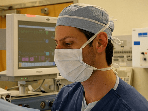 Photo: a medical professional wearing a surgical mask during an operation. Credit: Artur Bergman; Wikimedia Commons.