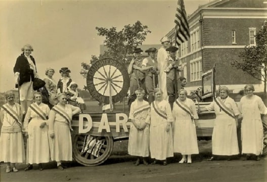 Photo: the D.A.R. in the 1922 July 4th parade. From the left to the right, the participants standing in front are: Mrs. Frank Corwith, Miss Betsy Bush, Mrs. C. E. Foster, Mrs. Lewis E. Downs, Mrs. Eli Fordham, Mrs. J. M. Jagger, Mrs. H. H. Hildreth, and Mrs. Raymond Corwith. From left to right onboard the float, the participants are: Mrs. R. Kendrick, Mrs. A. W. Tunnell, John M. Nugent as a child, Helen C. Bishop as a child, a young Edward. H. Foster, a young E. Halsey Howell, Adelaide Corwith, and a young Mercator Cooper Kendrick. Courtesy of the South Hampton Museum, South Hampton, New York.