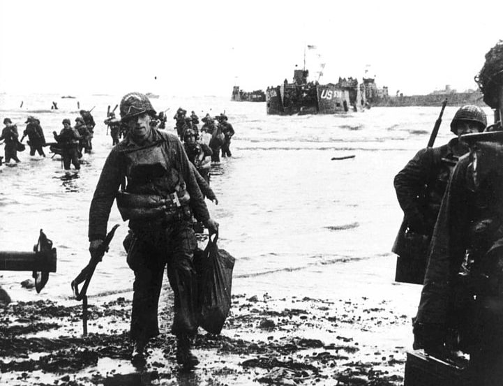 Photo: carrying full equipment, American assault troops move onto Utah Beach on the northern coast of France, 6 June 1944. Landing craft can be seen in the background. Credit: Wall; Wikimedia Commons.