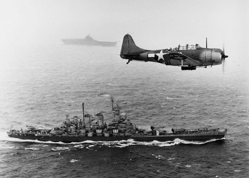 Photo: a U.S. Navy Douglas SBD-5 Dauntless of bombing squadron VB-16 flies an antisubmarine patrol low over the battleship USS Washington (BB-56) en route to the invasion of the Gilbert Islands, 12 November 1943. The ship in the background is USS Lexington (CV-16), the aircraft's home carrier. Note the depth charge below the SBD. Credit: U.S. Navy; Wikimedia Commons.