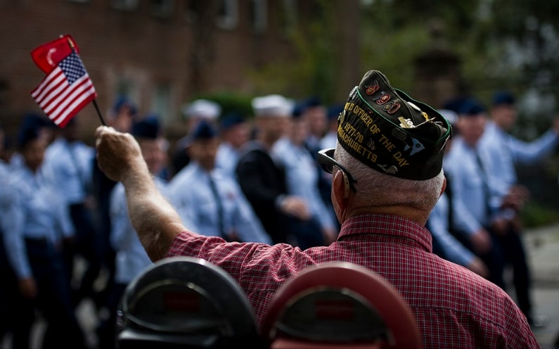 Photo: U.S. Marine Corps veteran Richard Starr waves an American flag as members of Joint Base Charleston march by while participating in the Ralph H. Johnson Veterans Hospital Annual Veterans Day parade 8 November 2014, in Charleston, S.C. Credit: Clayton Cupit; U.S. Air Force; Wikimedia Commons.